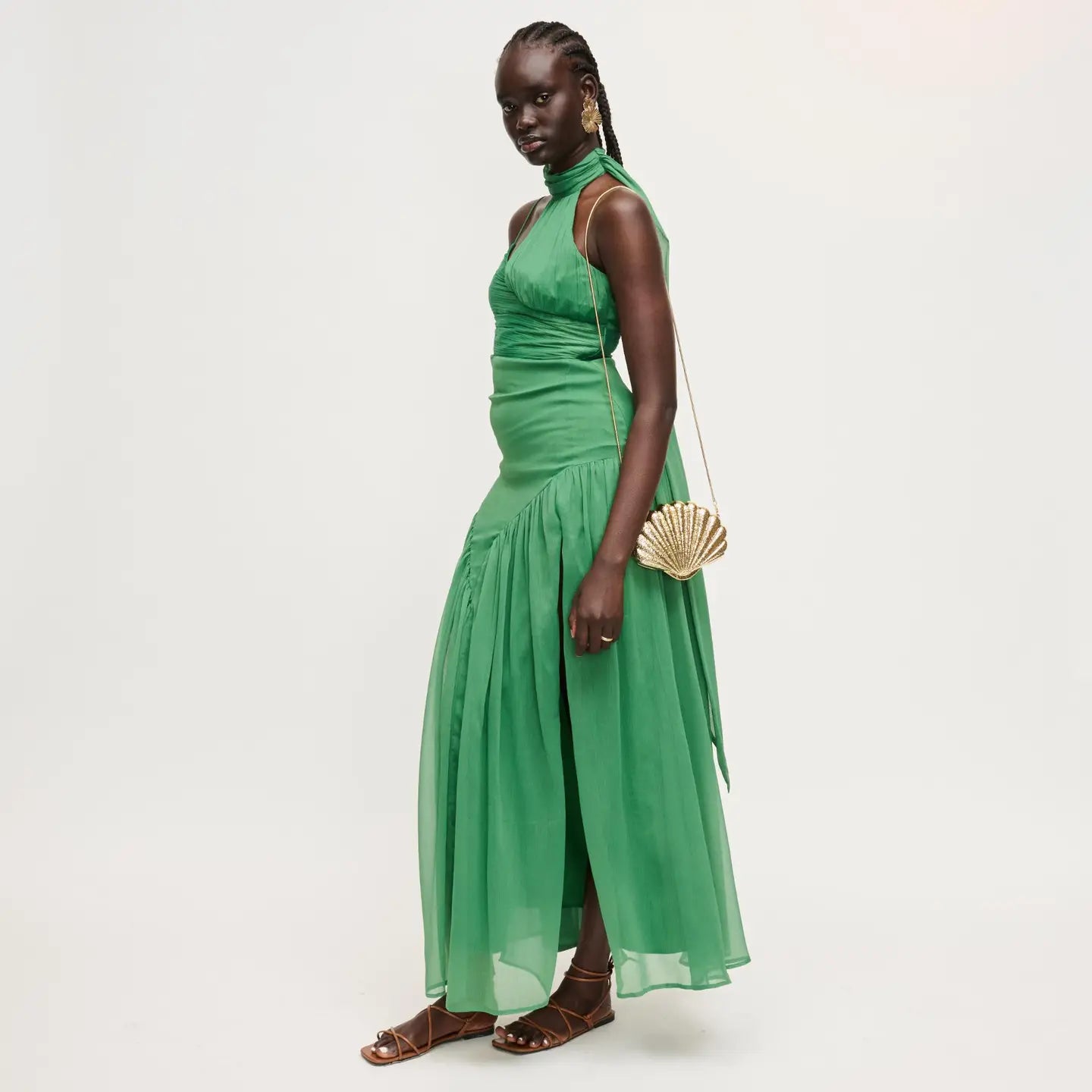 Woman wearing a green dress holding a gold clutch against a white background