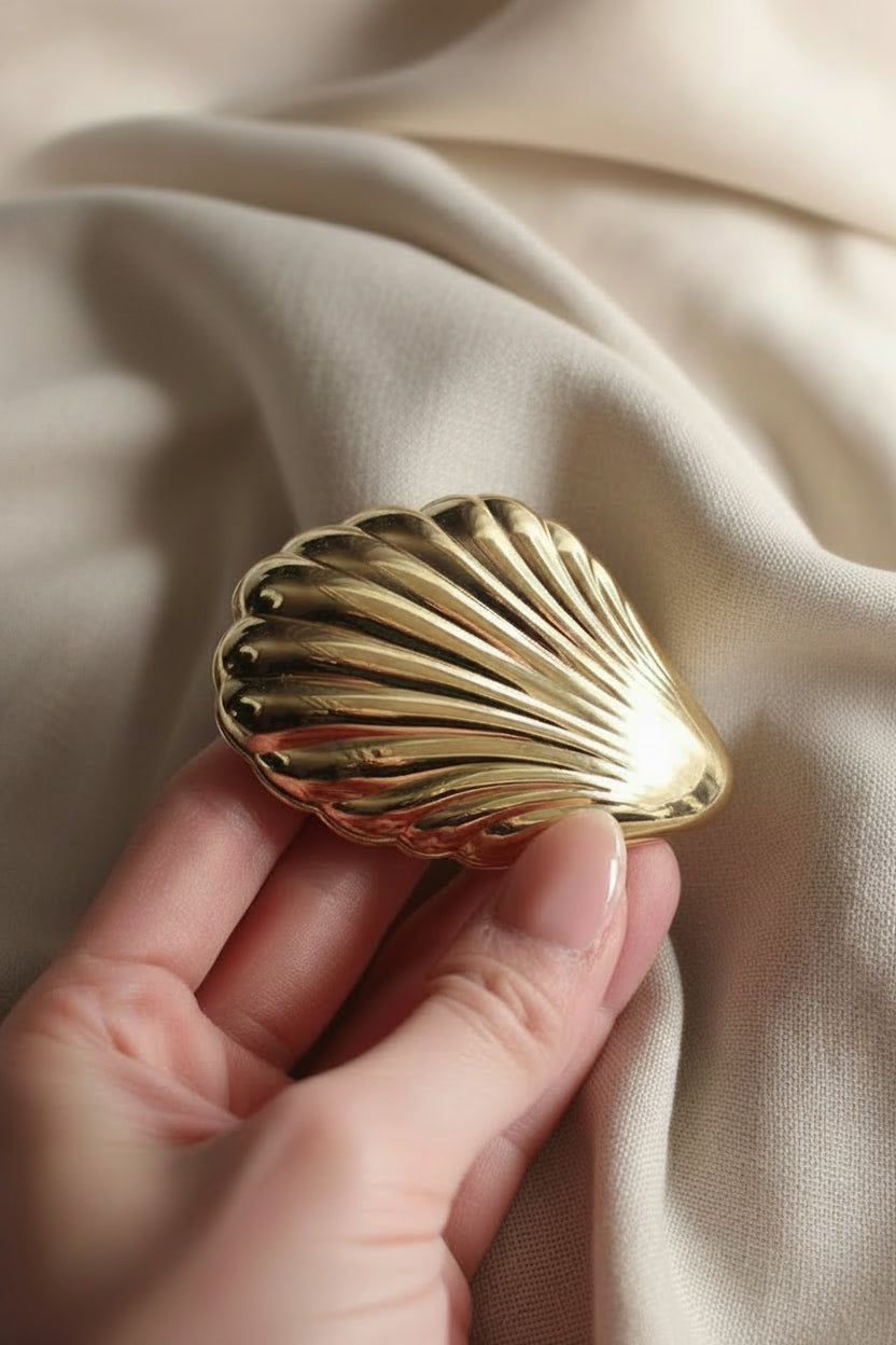 Gold shell-shaped jewelry box held by a hand on a white fabric background