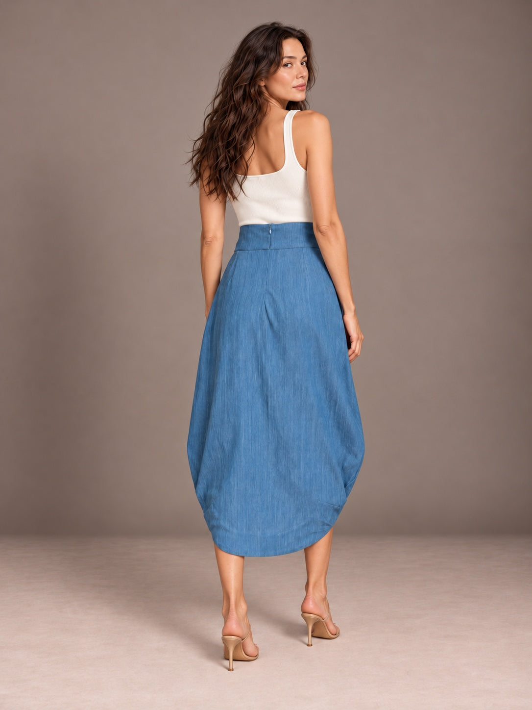 Back view of blue Cocoon Eco Denim wrap skirt styled with an ivory tank against a gray studio background