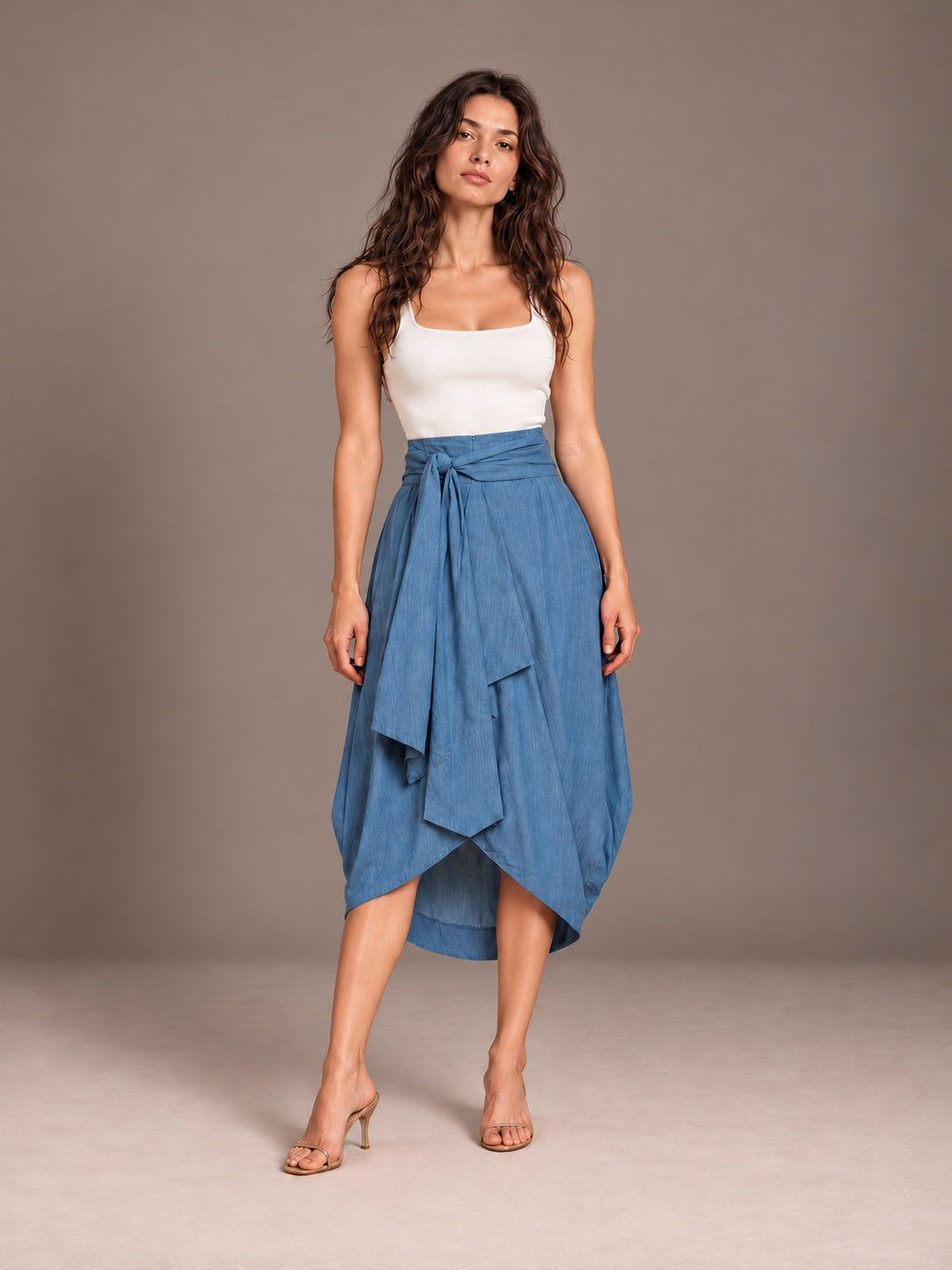 Front view of blue Cocoon Eco Denim wrap skirt styled with an ivory tank against a gray studio background