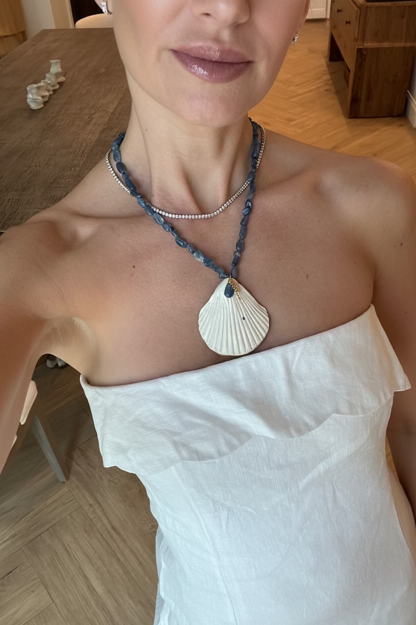 Person wearing a necklace with a large shell pendant on a wooden floor.