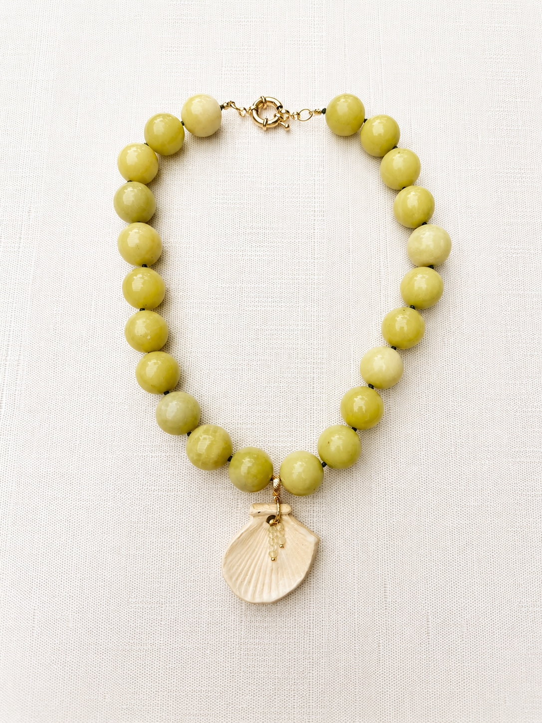 Necklace with green beads and a shell pendant on a white background