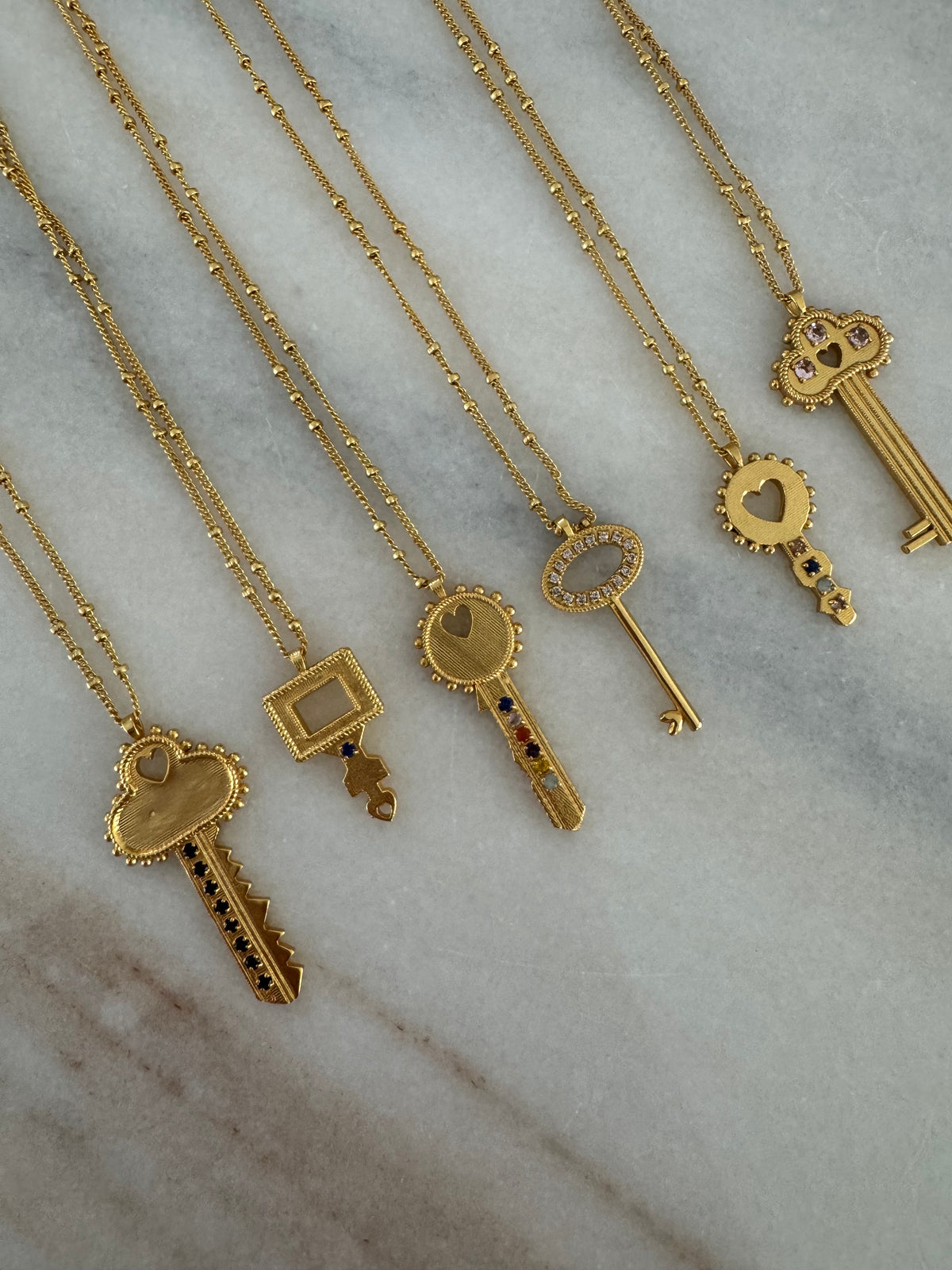 Gold necklaces with various KEY pendants on a marble surface