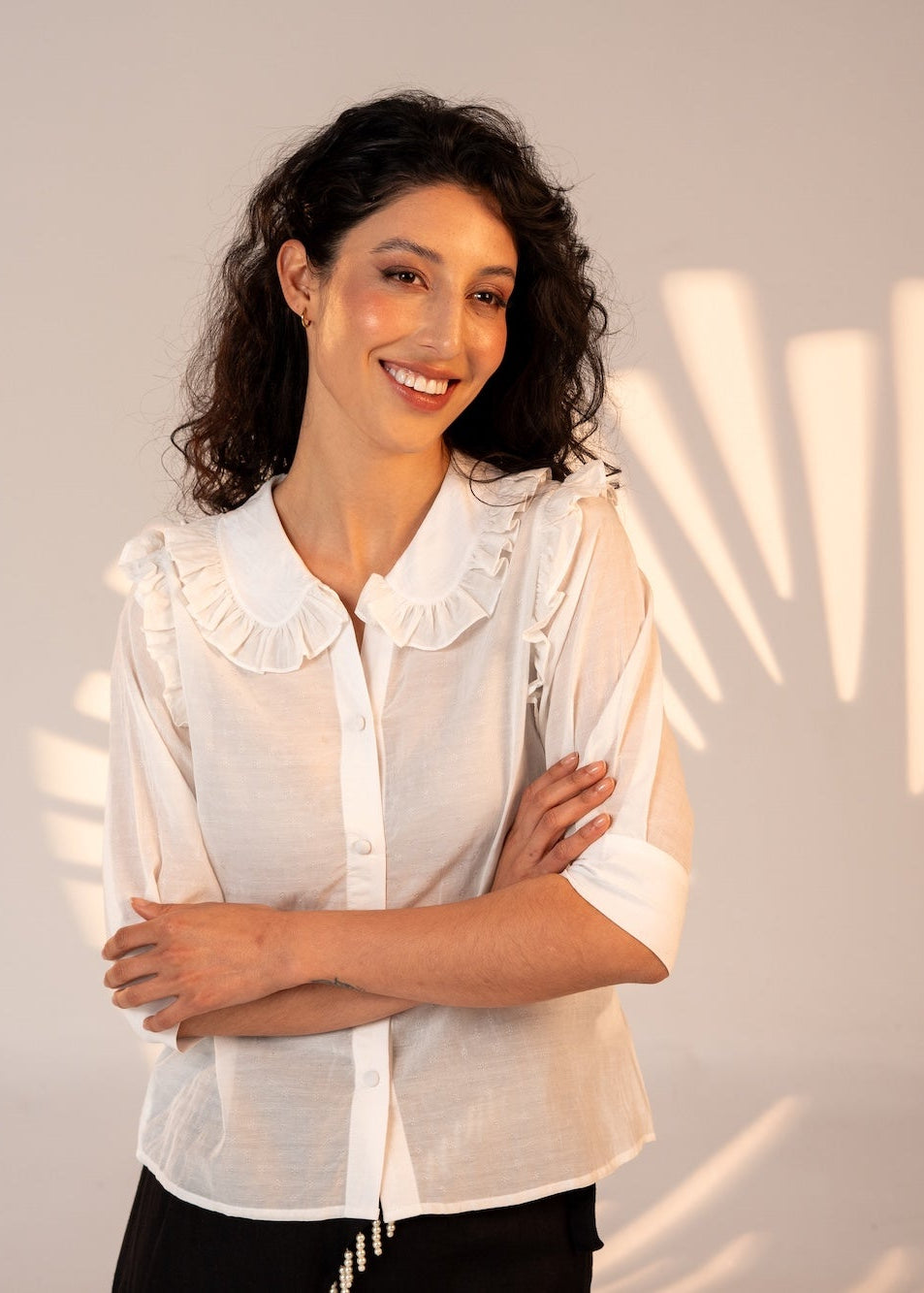 Woman wearing a white blouse with ruffled collar against a light gray background