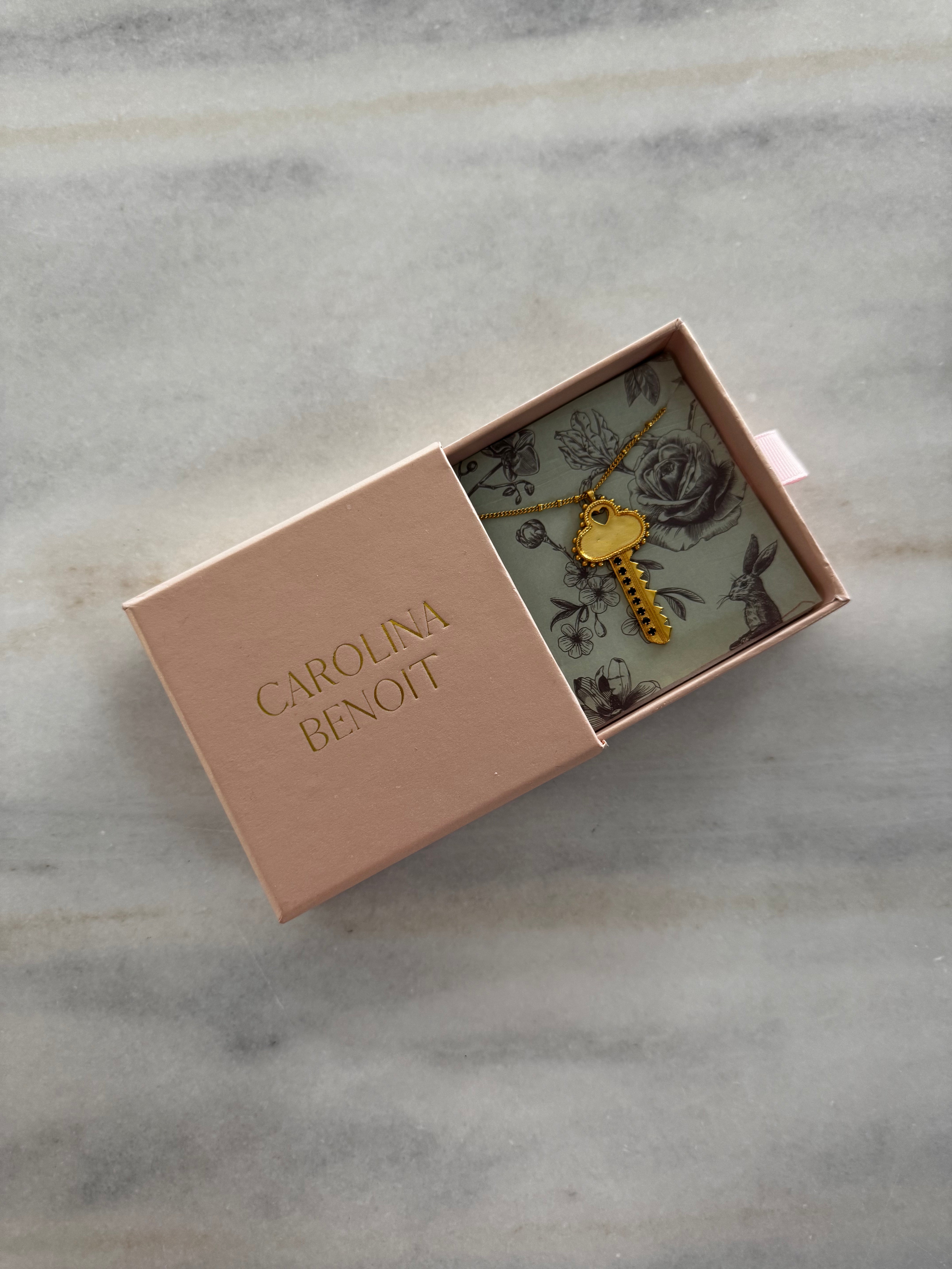 Gold heart-shaped key pendant in a 'Carolina Benoit' box on a marble surface
