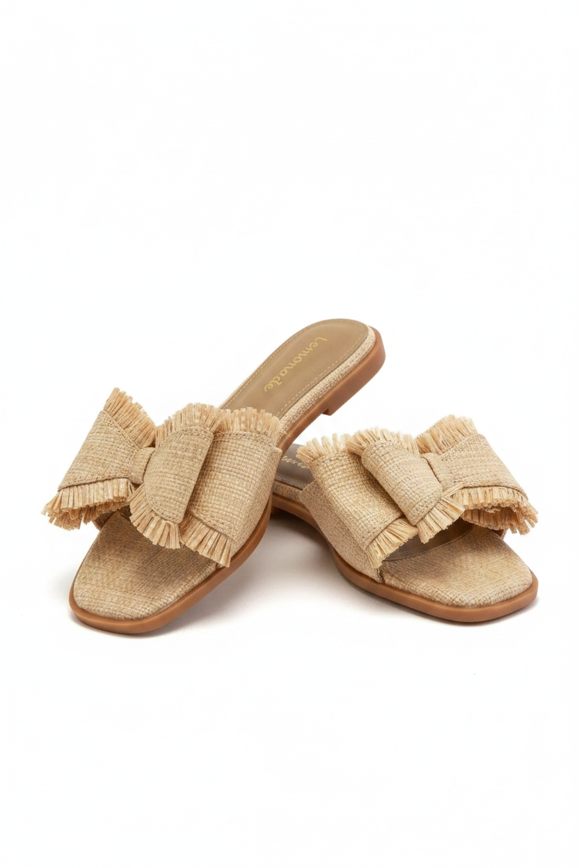 Pair of beige sandals with ruffled bow details on a beige background