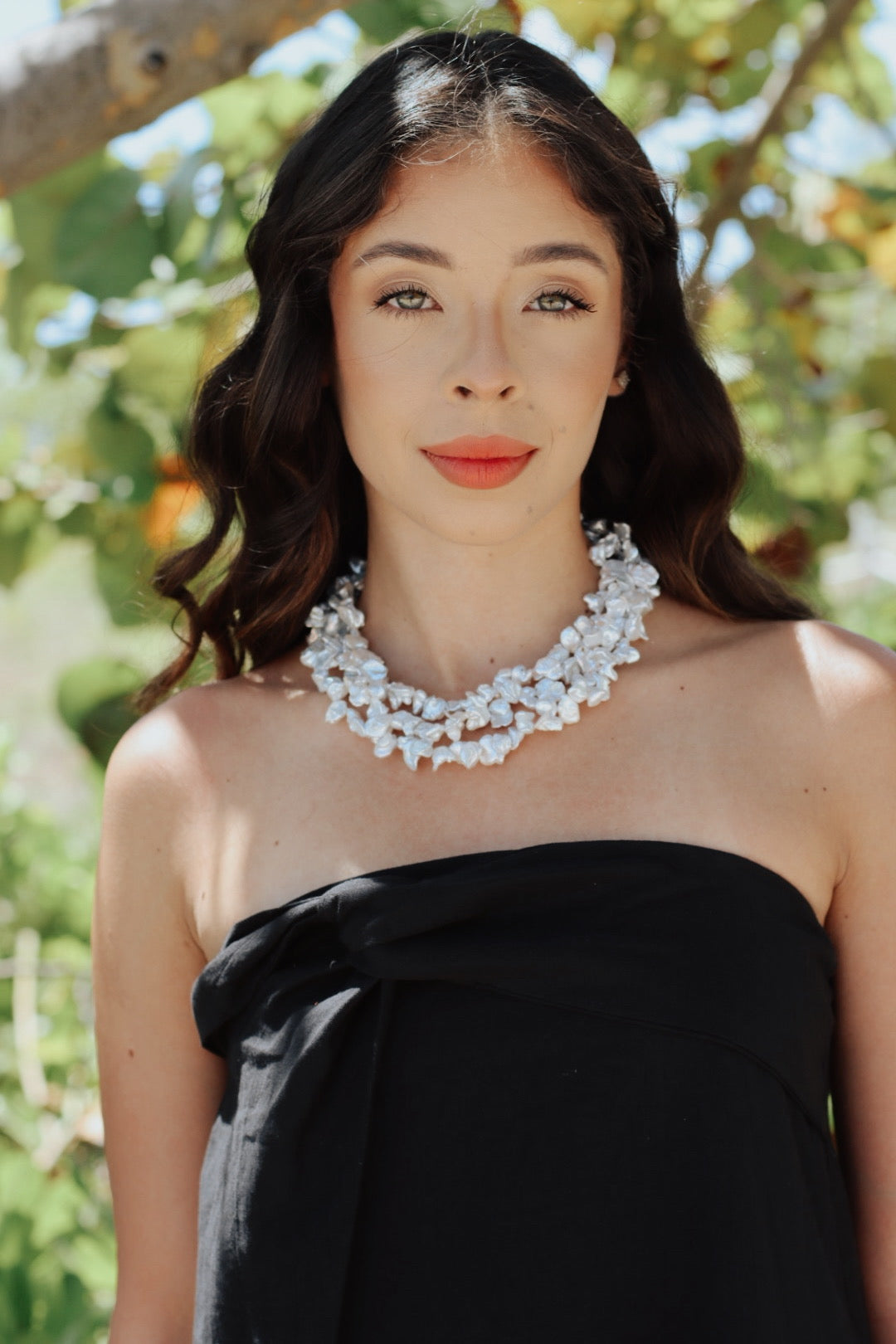 Woman wearing the Baroque Garden Necklace, a bold layered baroque pearl choker, styled with a black strapless dress in a natural outdoor setting