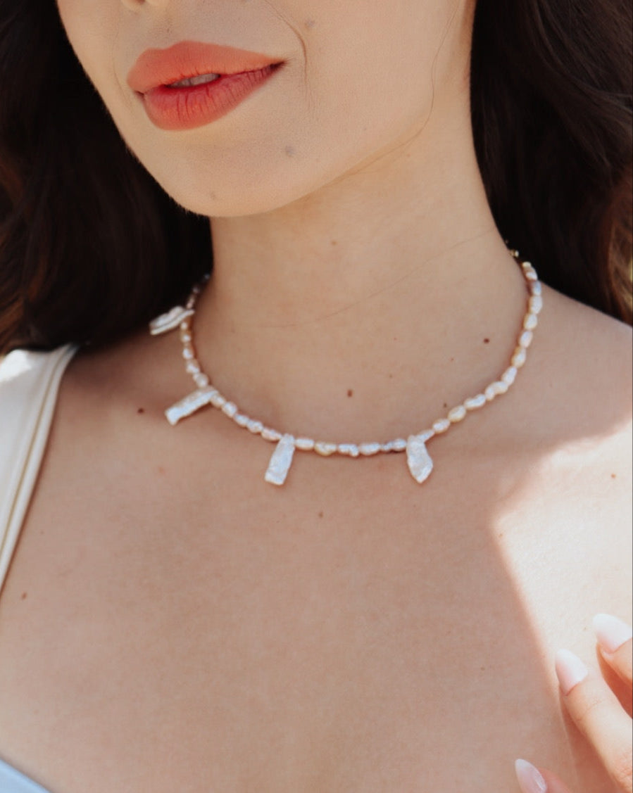 Handmade vintage freshwater pearl choker necklace with irregular long pearls and gold-plated clasp, styled on natural linen background.