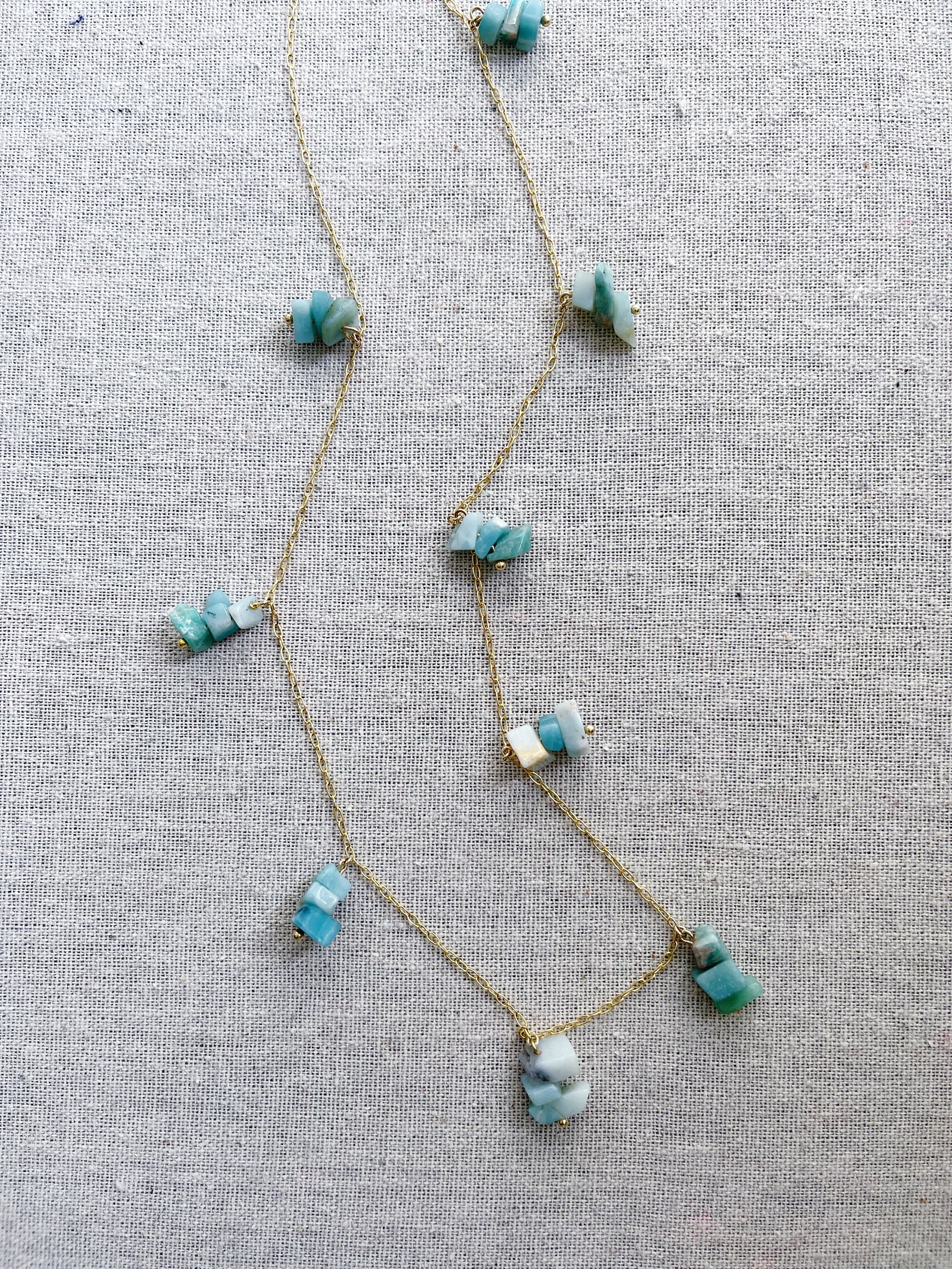 A gold necklace featuring groups of aquamarine stones. The aquamarine stone is used in holistic healing and crystal therapy. Spiritually, aquamarine is associated with trusting and letting go. In ancient times, aquamarine was believed to be the treasure of mermaids. Sailors used the stone as a talisman to bring good luck on the open waters. The gem was used as a symbol of protection and fearlessness too. Aquamarine 14k plated gold chain 30” long