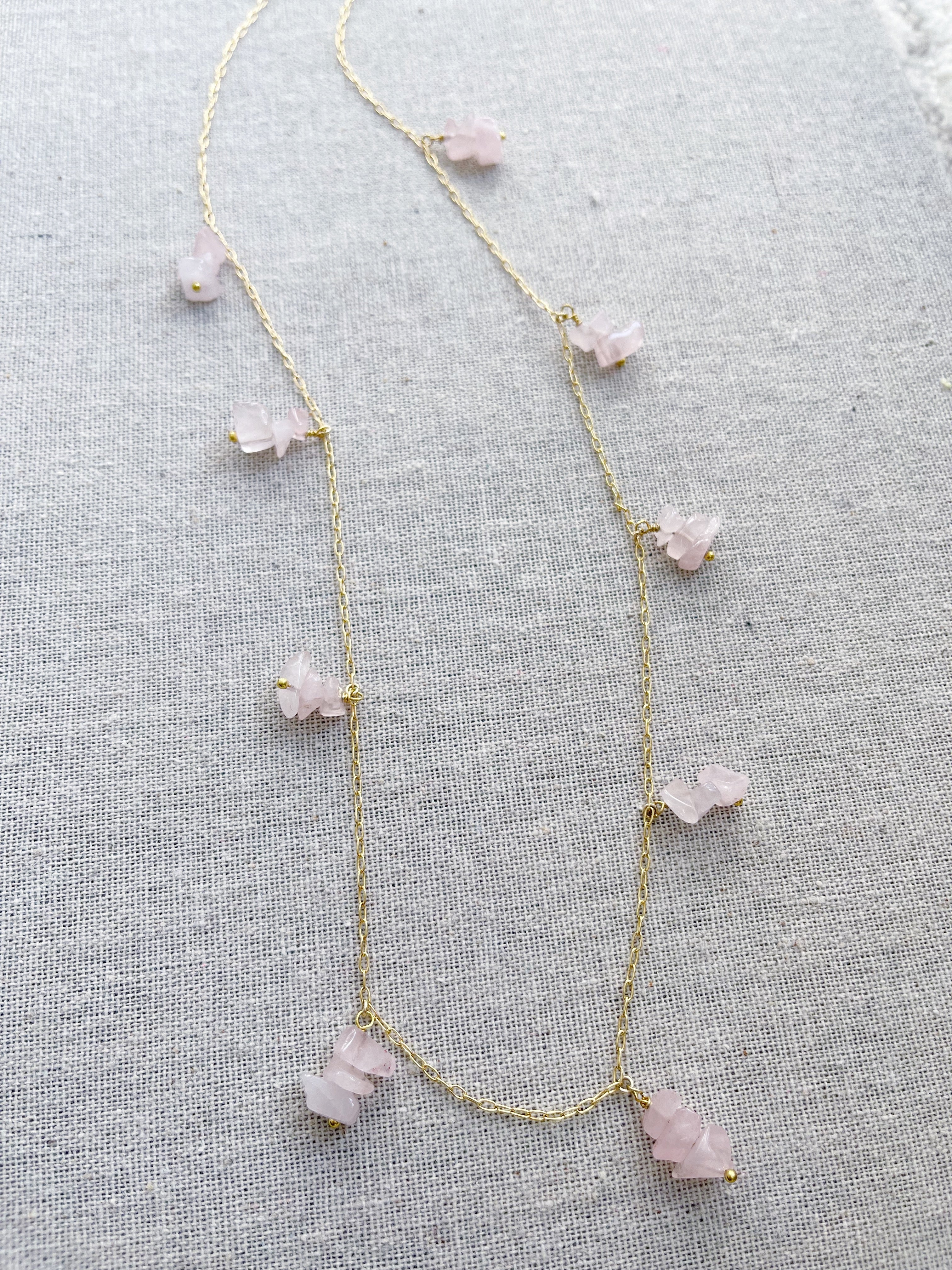 A gold necklace featuring groups of pink quartz stones. The pink quartz stone is used in holistic healing and crystal therapy. Rose quartz is known as a healing crystal and the stone of unconditional love. It's believed by some to emit strong vibrations of love, which are thought to: support emotional and relationship healing. inspire compassion. Pink quartz 14k plated gold chain