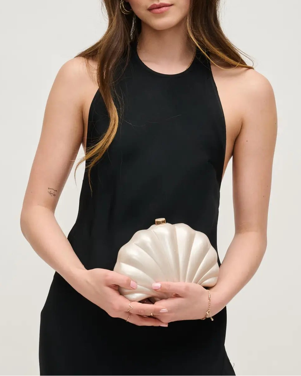 Woman holding a shell-shaped clutch against a plain background