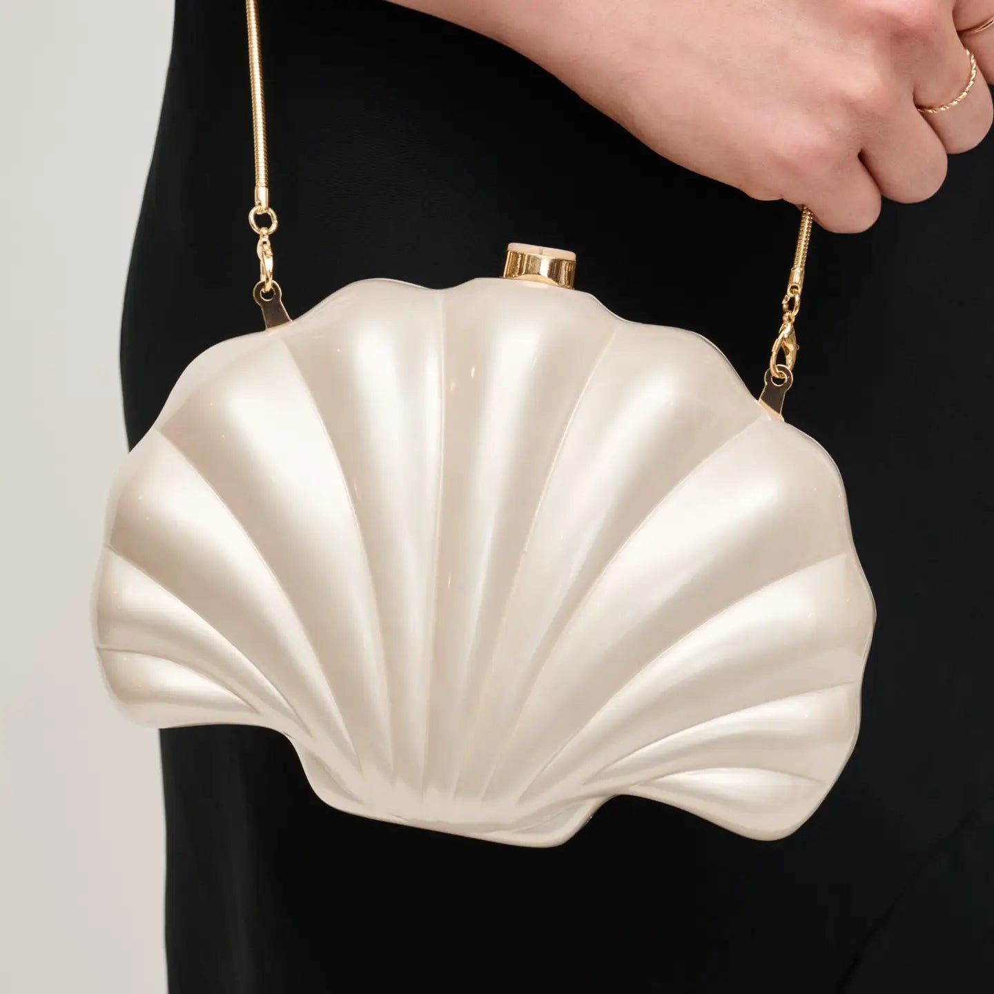 Shell-shaped handbag held by a person against a neutral background