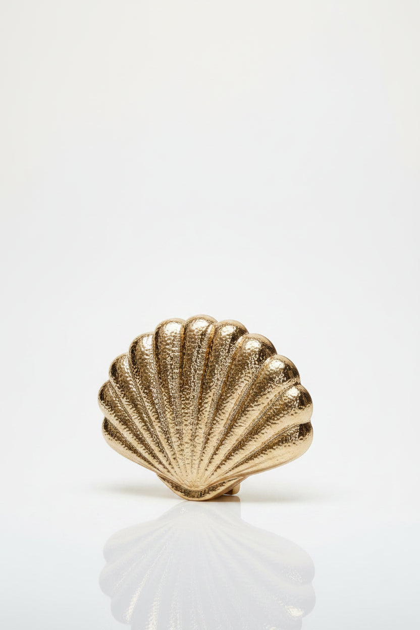 Gold shell-shaped clutch held by hands against a green background