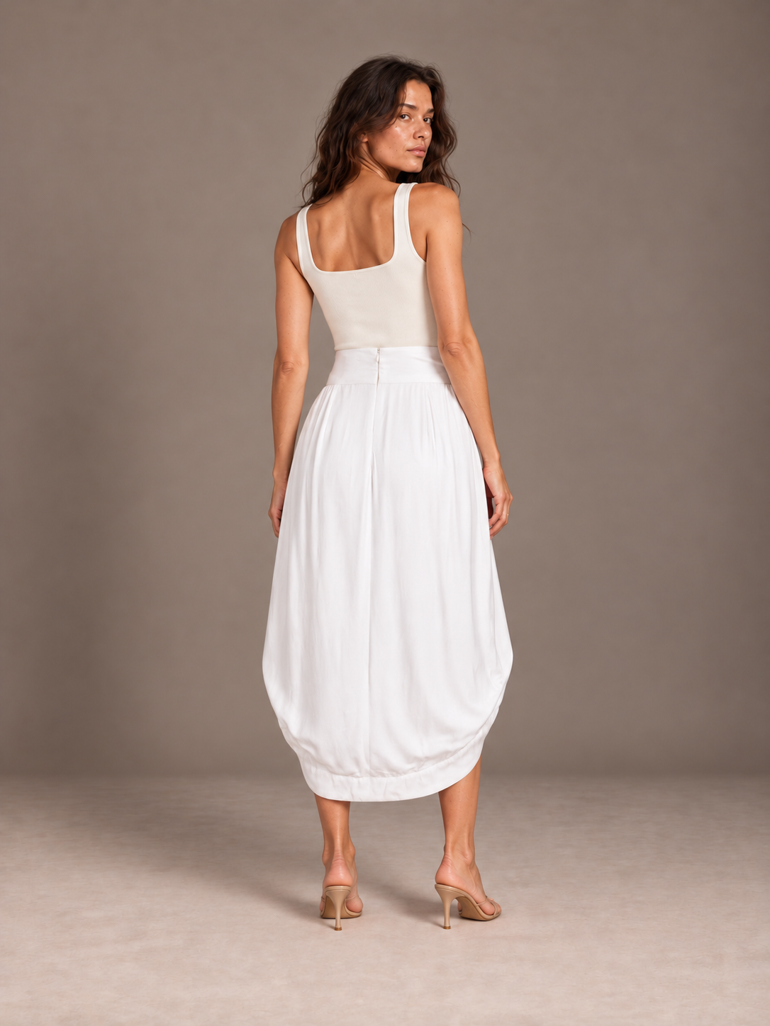 Back view of the white Cocoon Bamboo Bow Skirt showing its rounded drape and longer back hem in a gray studio