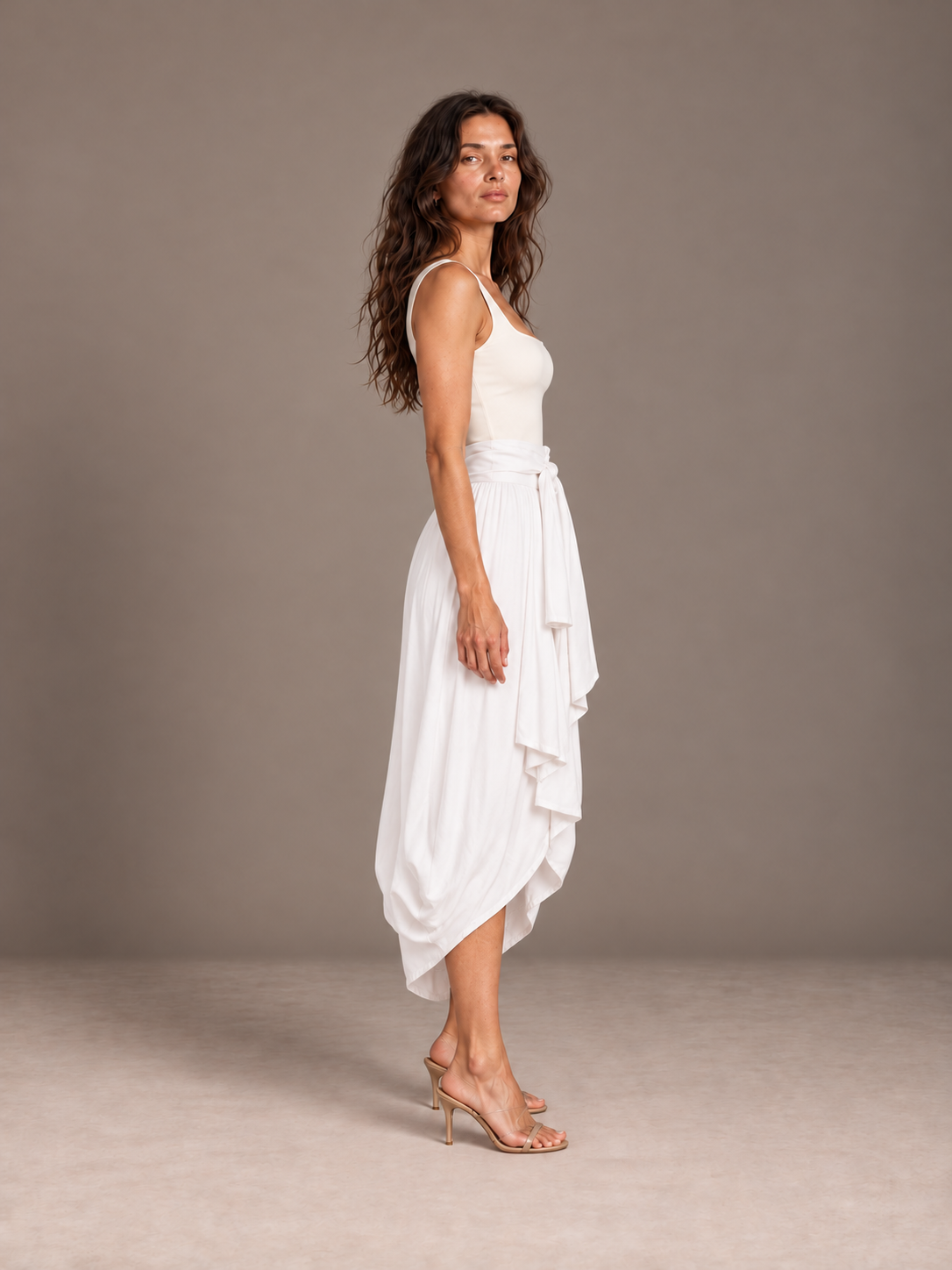 Side view of the white Cocoon Bamboo Bow Skirt showing its close cocoon drape and high-low hem in a gray studio