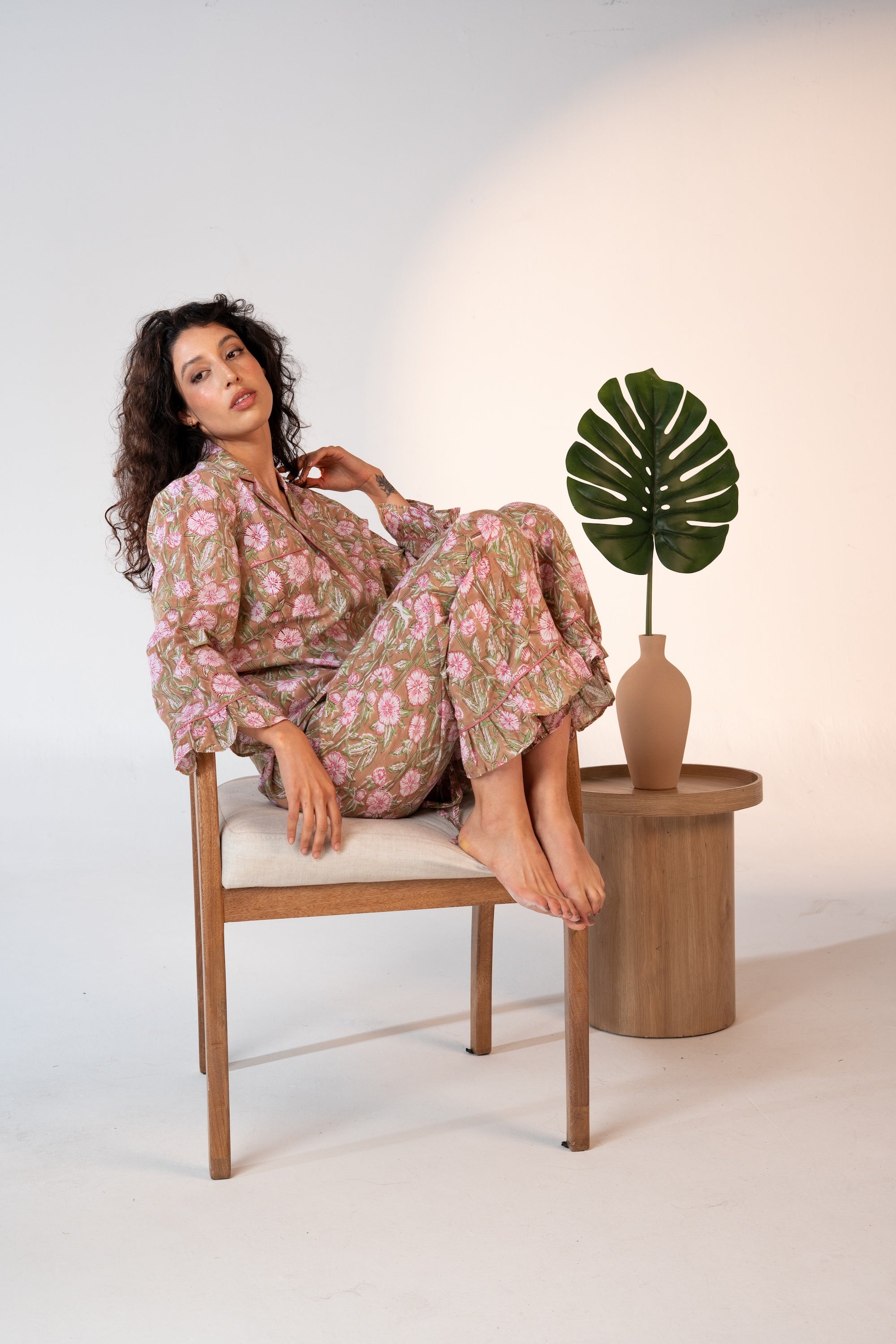 Woman in a floral dress sitting on a chair next to a plant in a studio setting