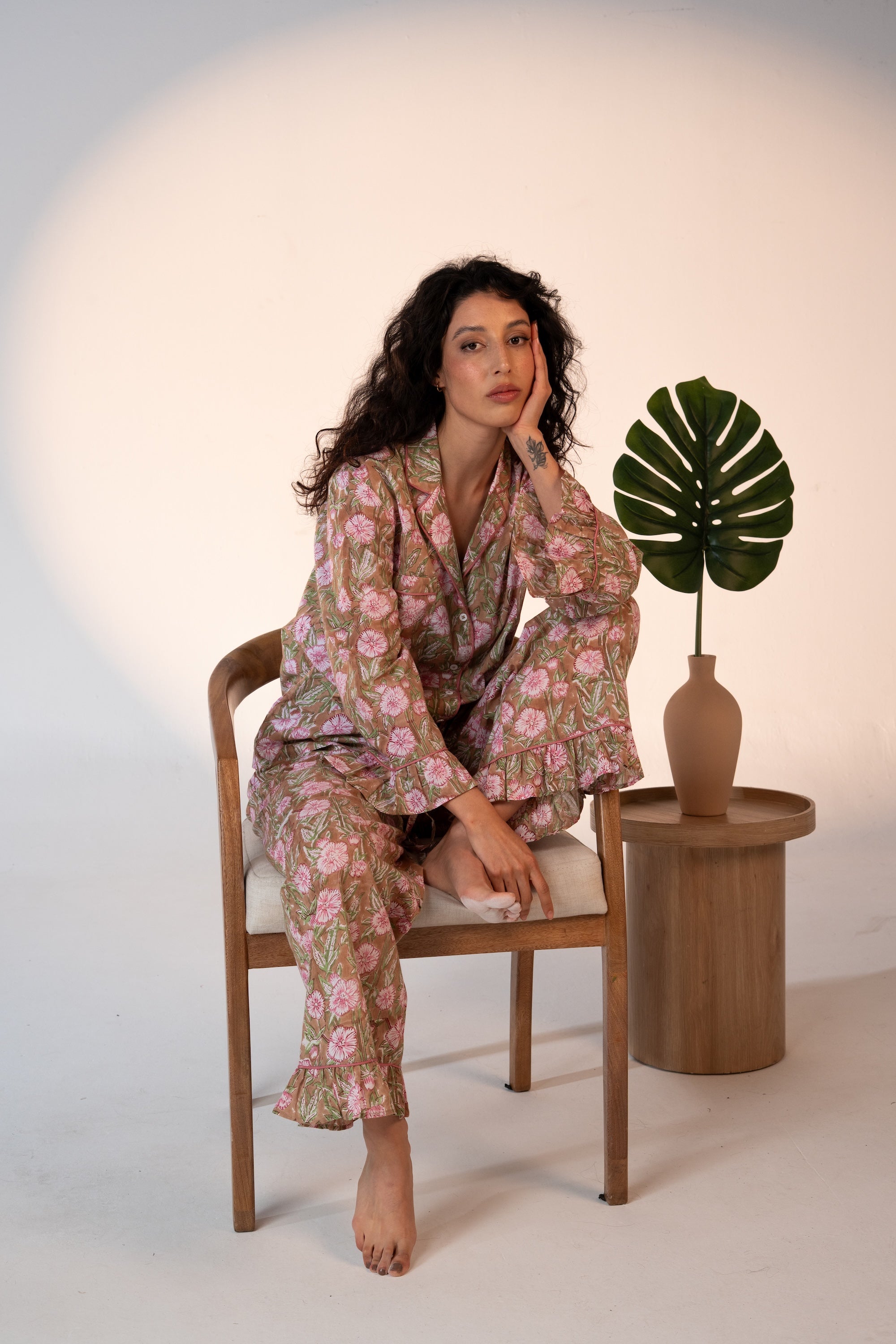 Woman in a floral outfit sitting on a chair with a plant in the background