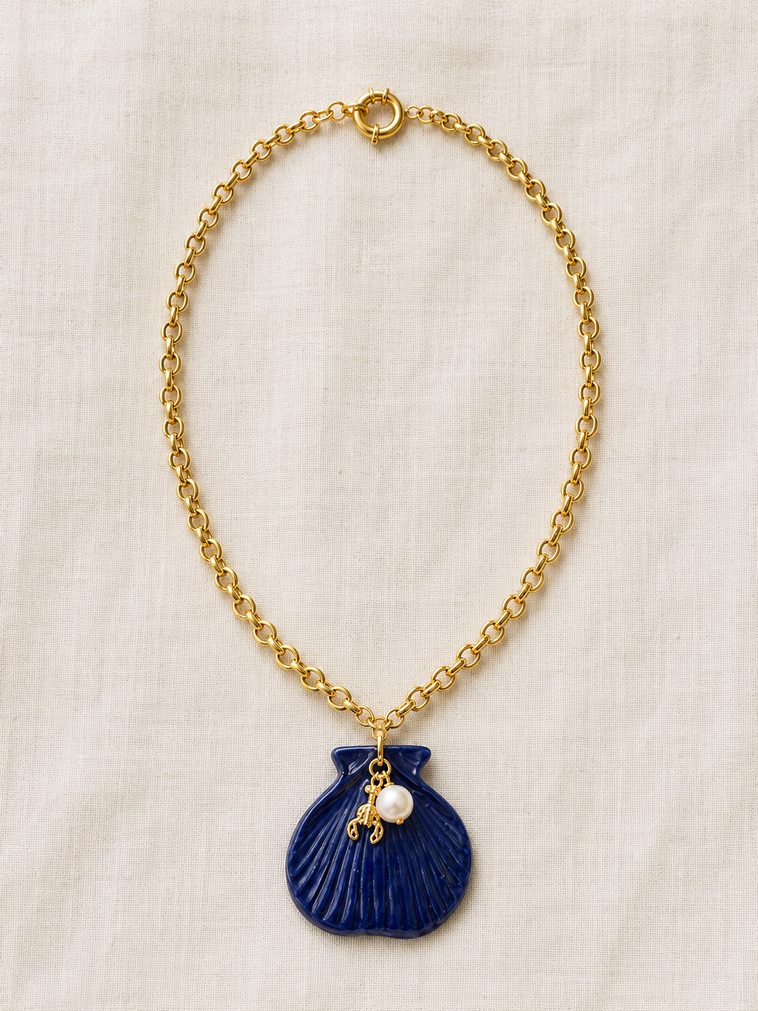 Gold chain necklace with a blue pendant and pearl on a beige background