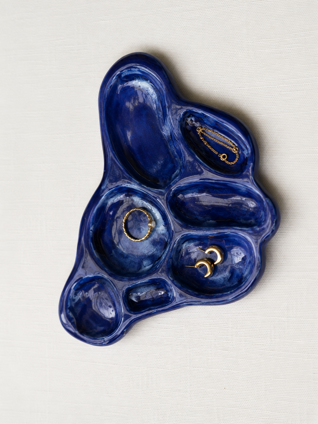 Blue ceramic jewelry organizer with gold jewelry on a white background