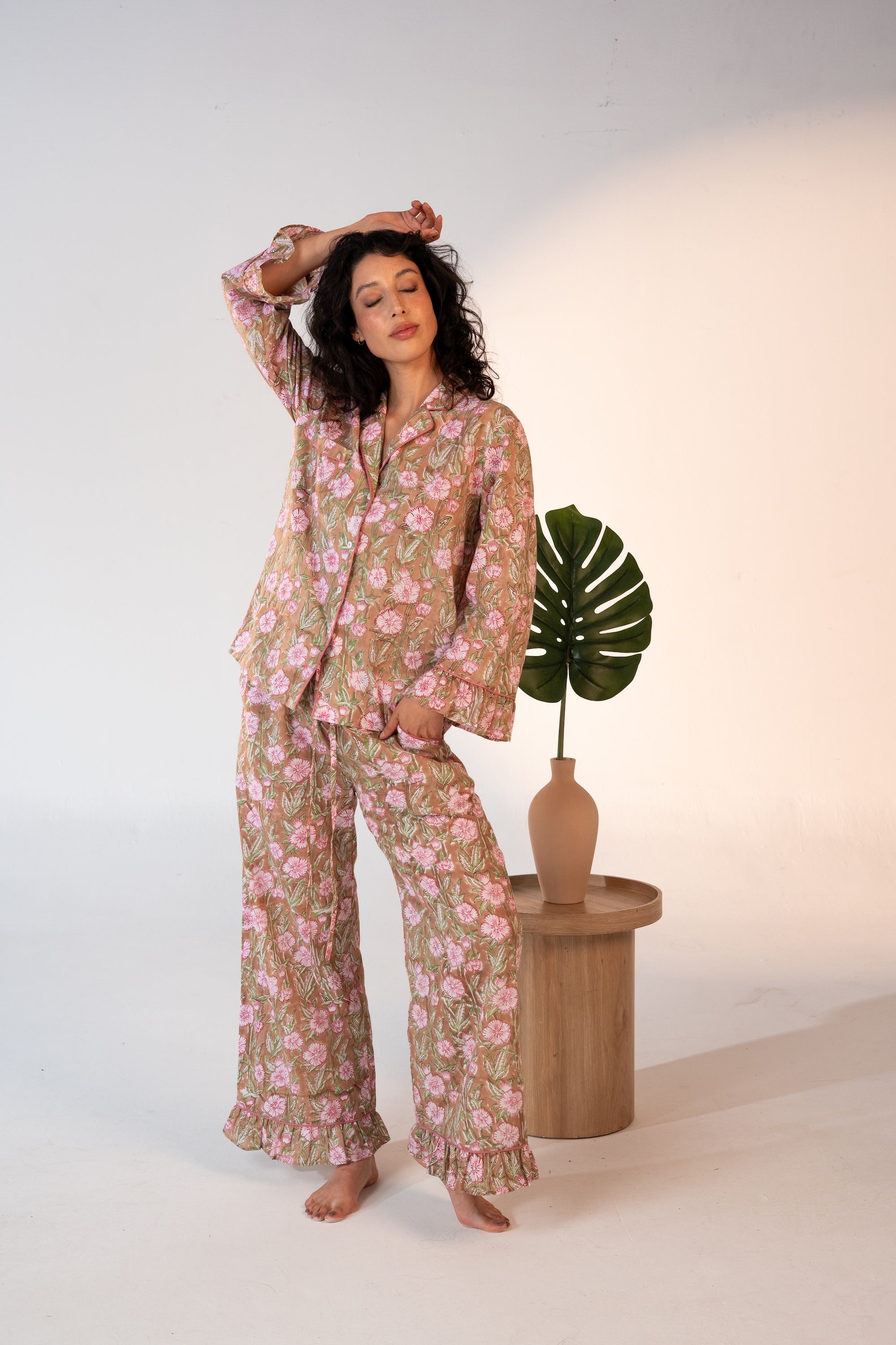 Woman wearing a floral pajama set standing next to a wooden stool with a plant.