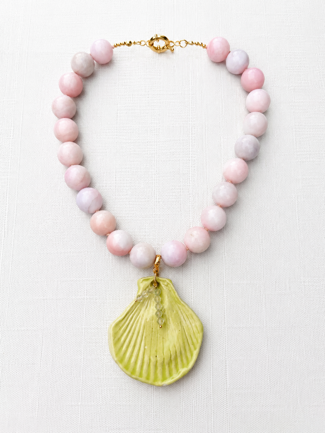 Necklace with pink beads and a yellow shell pendant on a white background