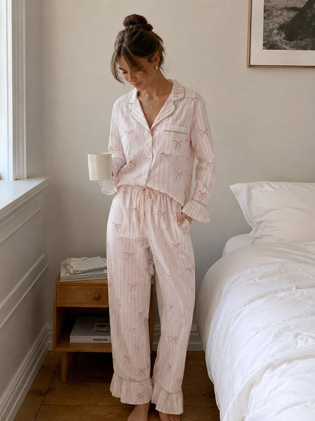 Woman in pink pajama set standing in a bedroom holding a mug.