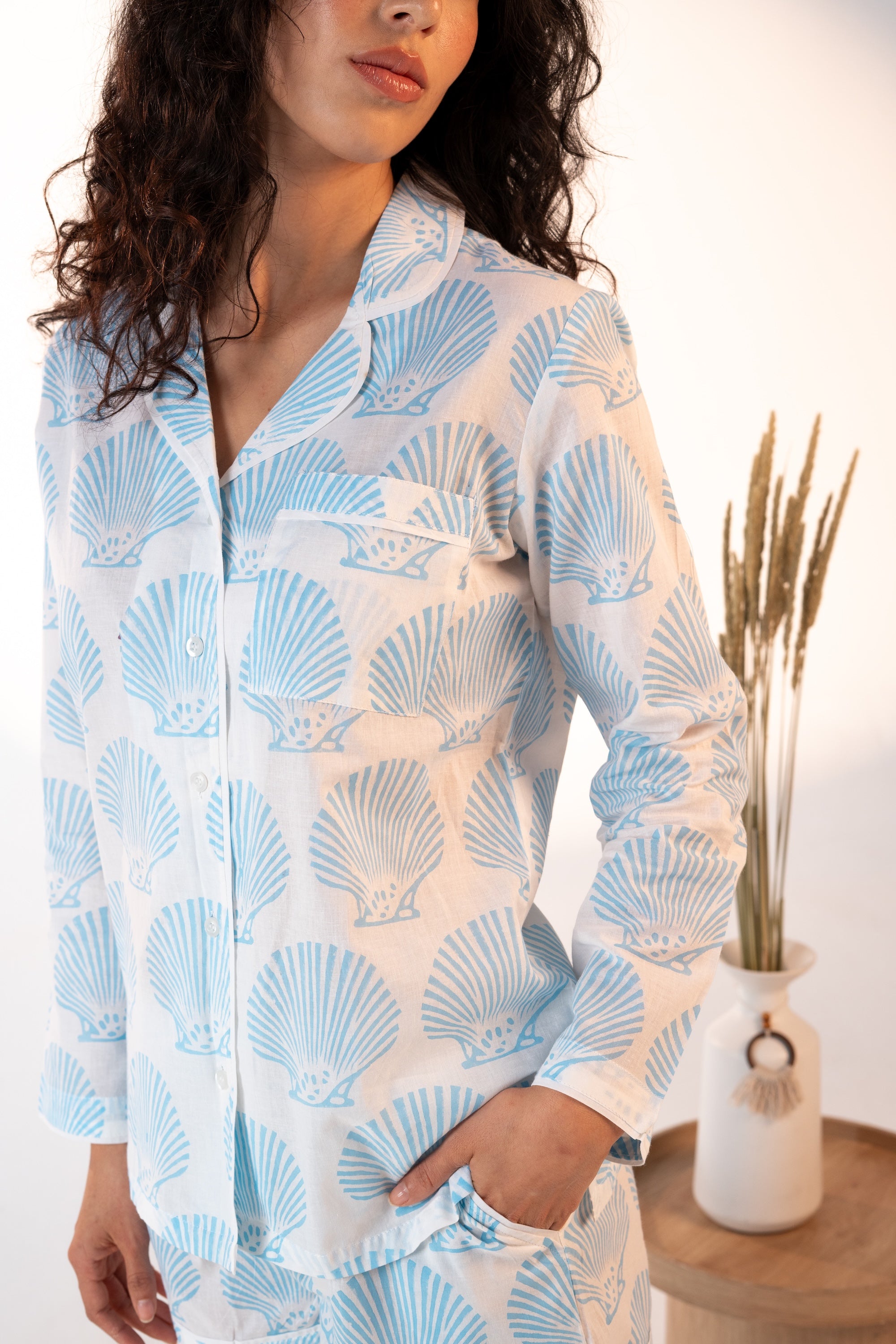 Woman wearing a blue and white shell patterned shirt with a white background and plant decor.