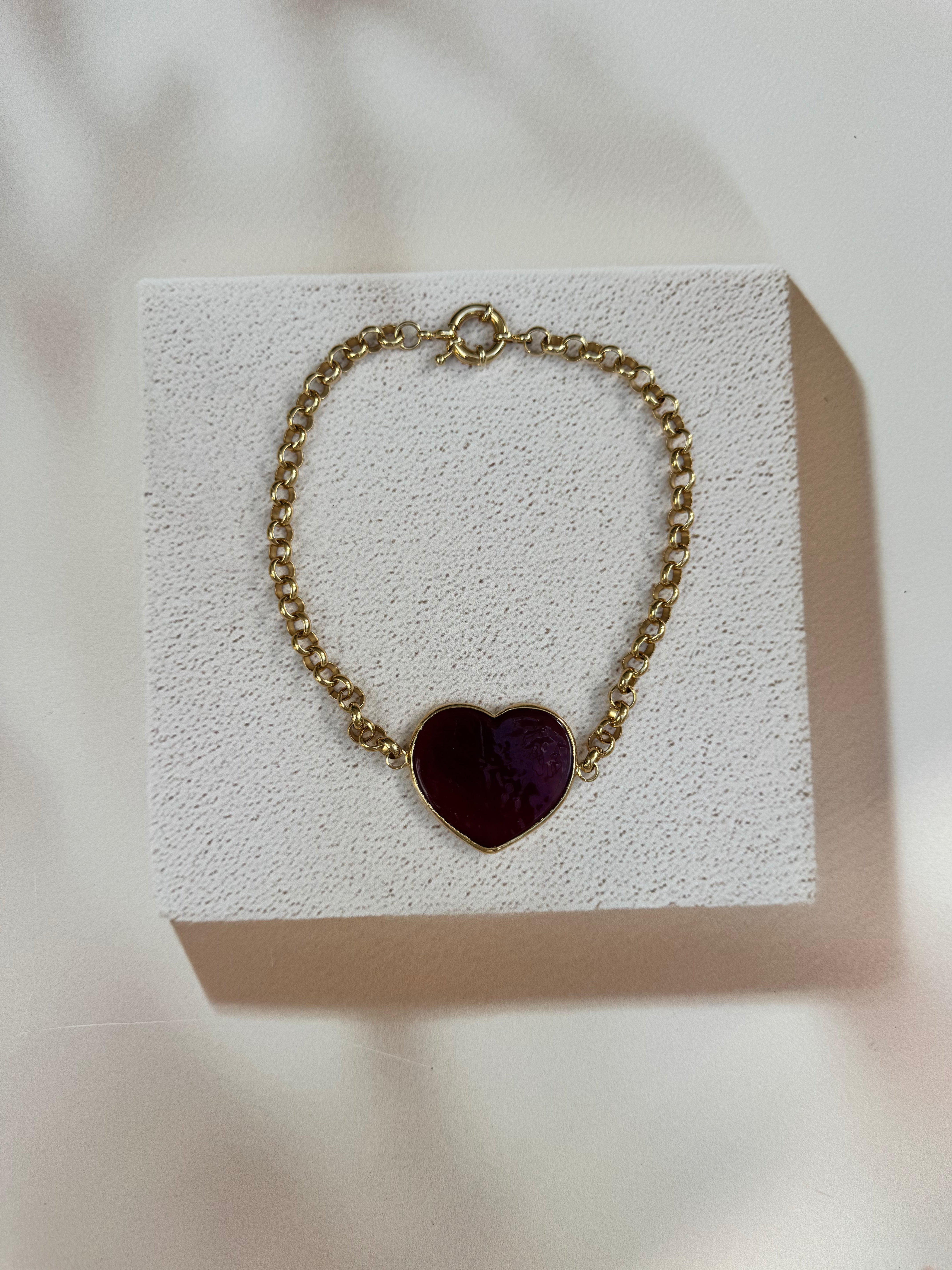 Gold chain necklace with a heart-shaped purple pendant on a textured white surface.