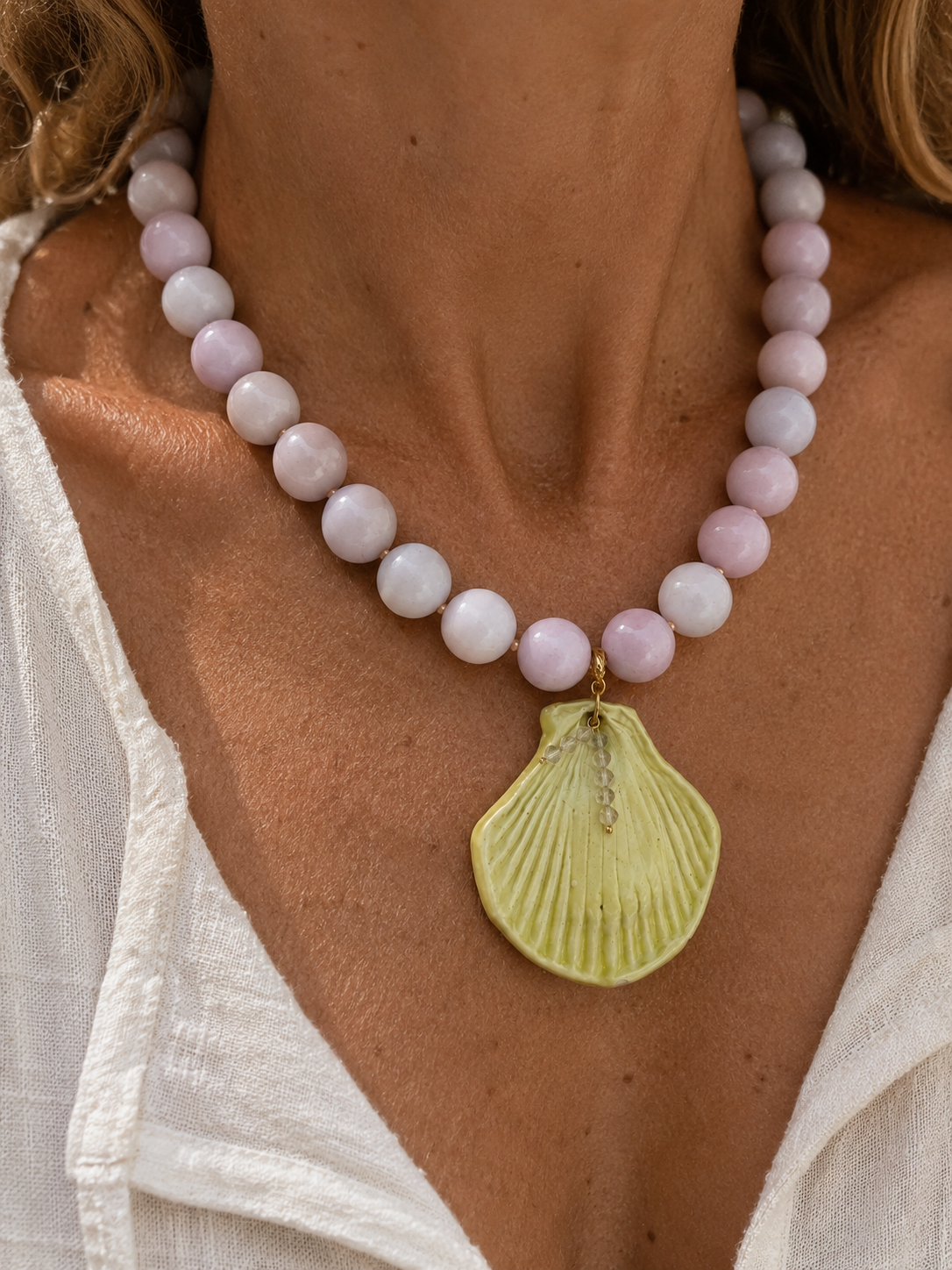 Necklace with pink beads and a yellow shell pendant on a person wearing a white top.