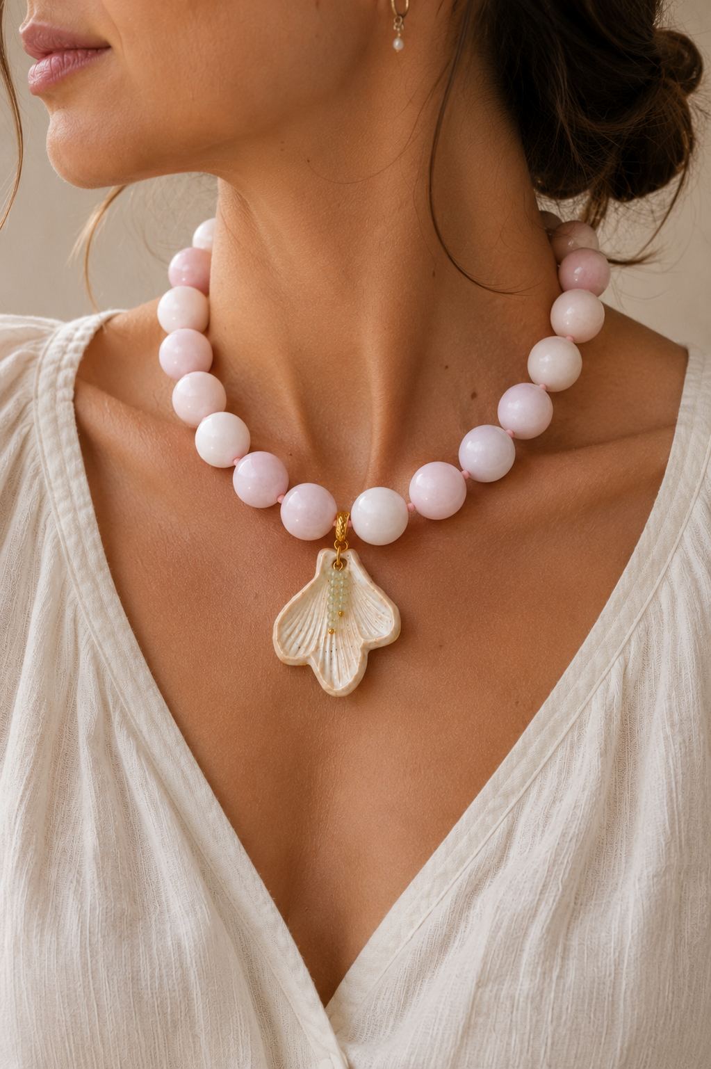 Necklace with pink beads and a leaf-shaped pendant worn by a person in a white top.
