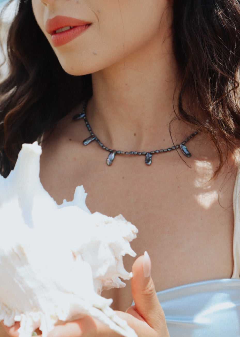 Woman wearing vintage pearl choker necklace, layered with gold chains, showcasing neckline styling.