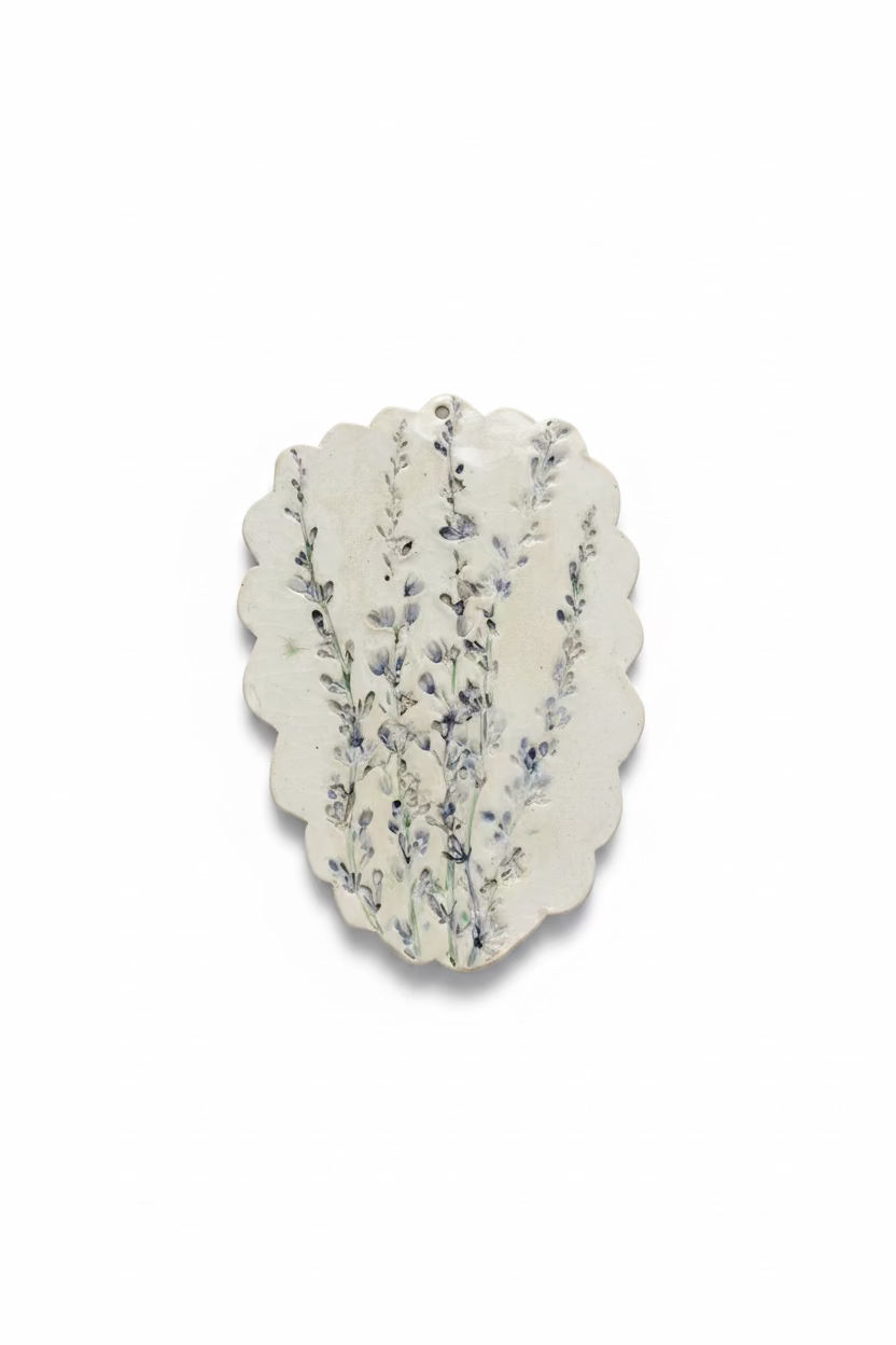 An irregularly shaped, scalloped-edge ceramic plate or tray with a blue floral pattern on a textured off-white glaze, displayed against a light gray fabric background.