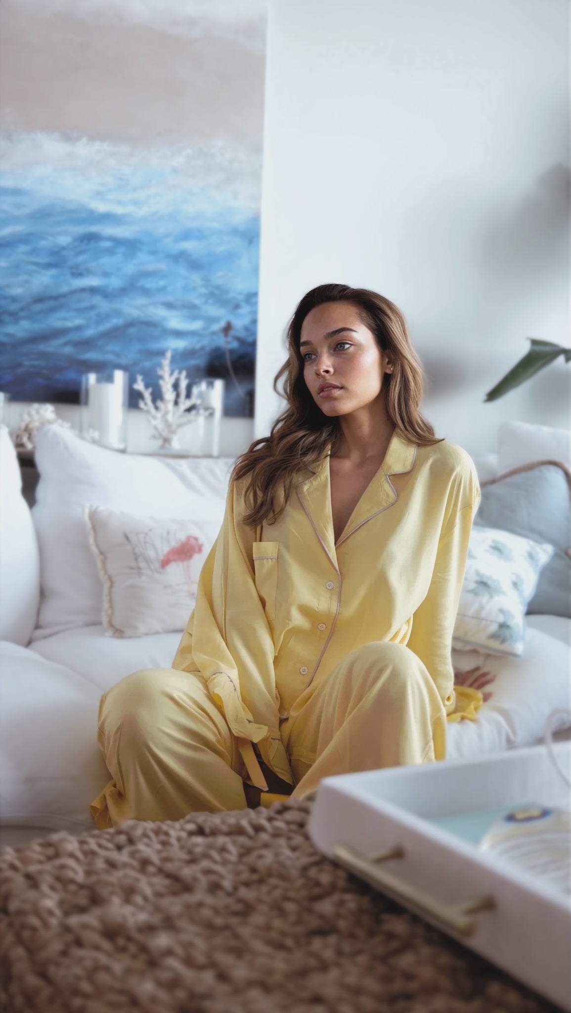 Woman in yellow pajamas sitting on a couch with a scenic painting in the background