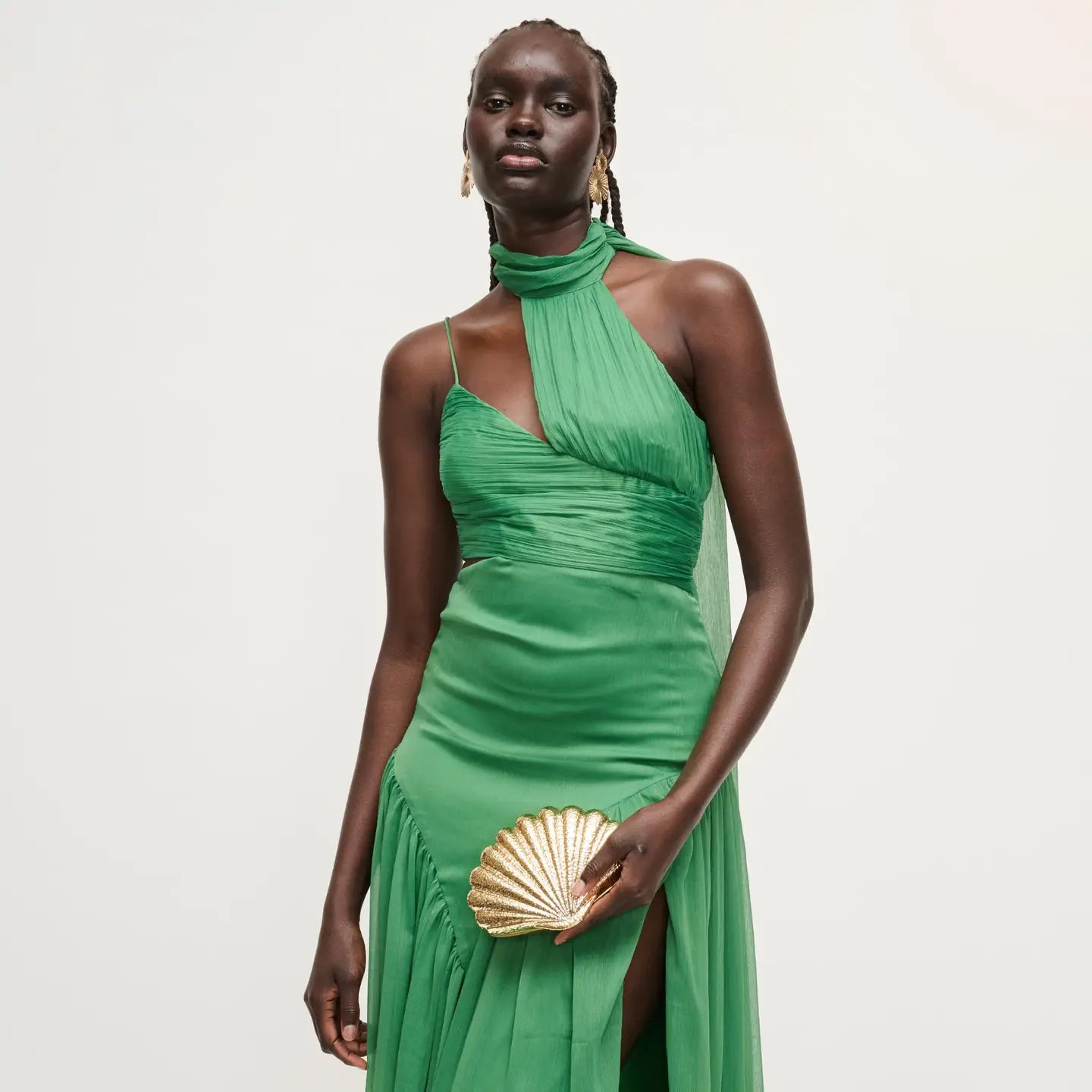 Woman wearing a green dress holding a gold clutch against a white background