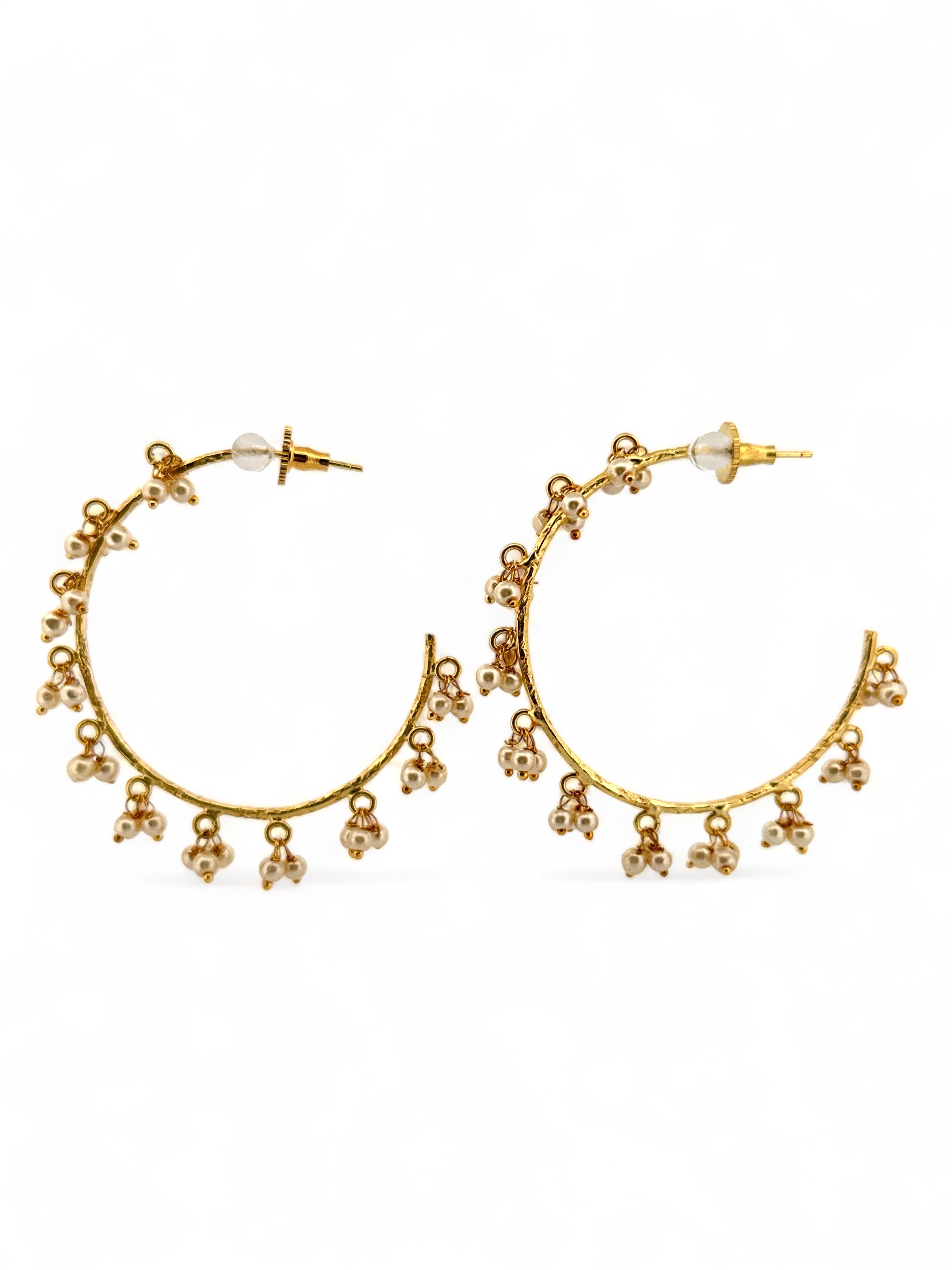 Close-up of 14k gold-plated hoop earrings adorned with beige pearls, displayed on a neutral background