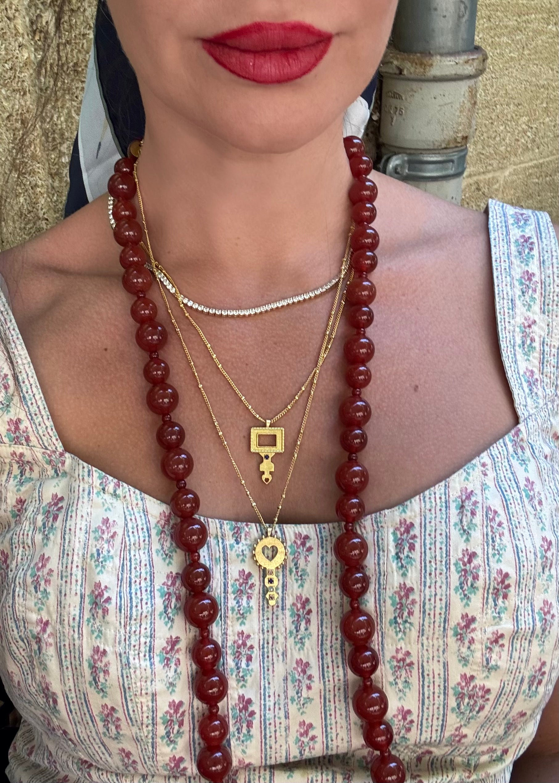 Close-up of a person wearing a long red beaded necklace and gold jewelry.