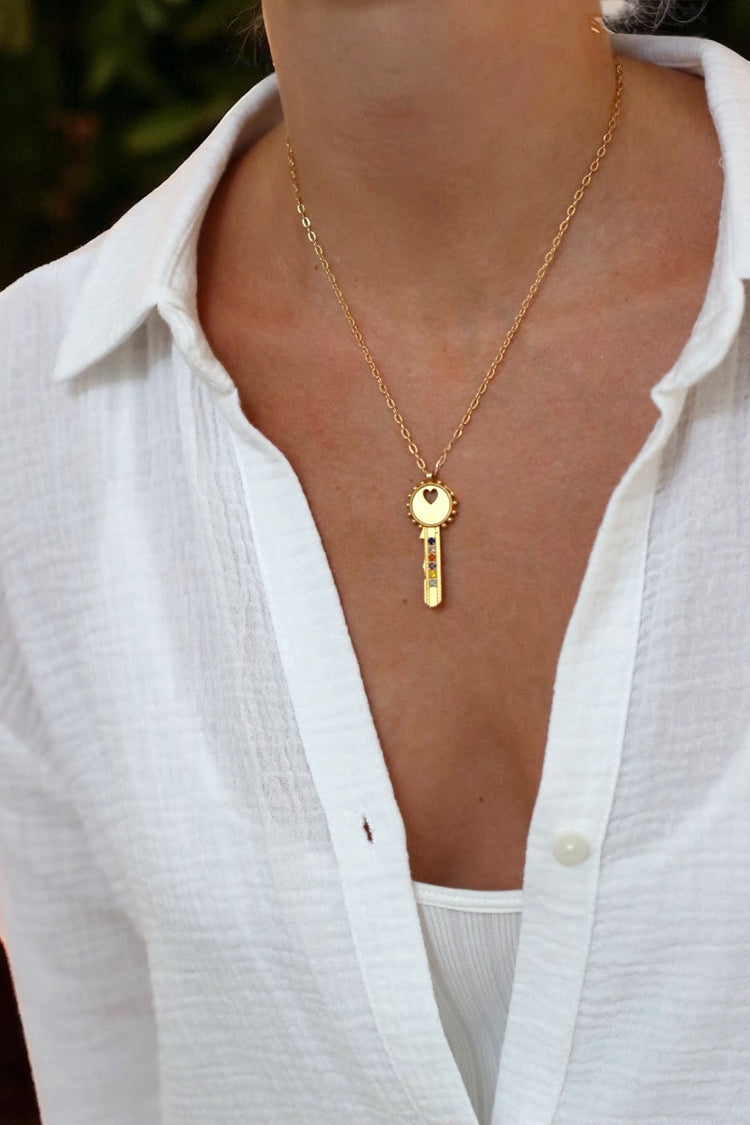Gold necklace with a key pendant worn by a person in a white shirt.