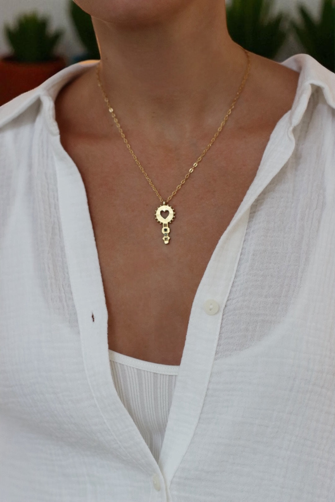 Gold necklace with a heart-shaped pendant worn by a person in a white shirt.