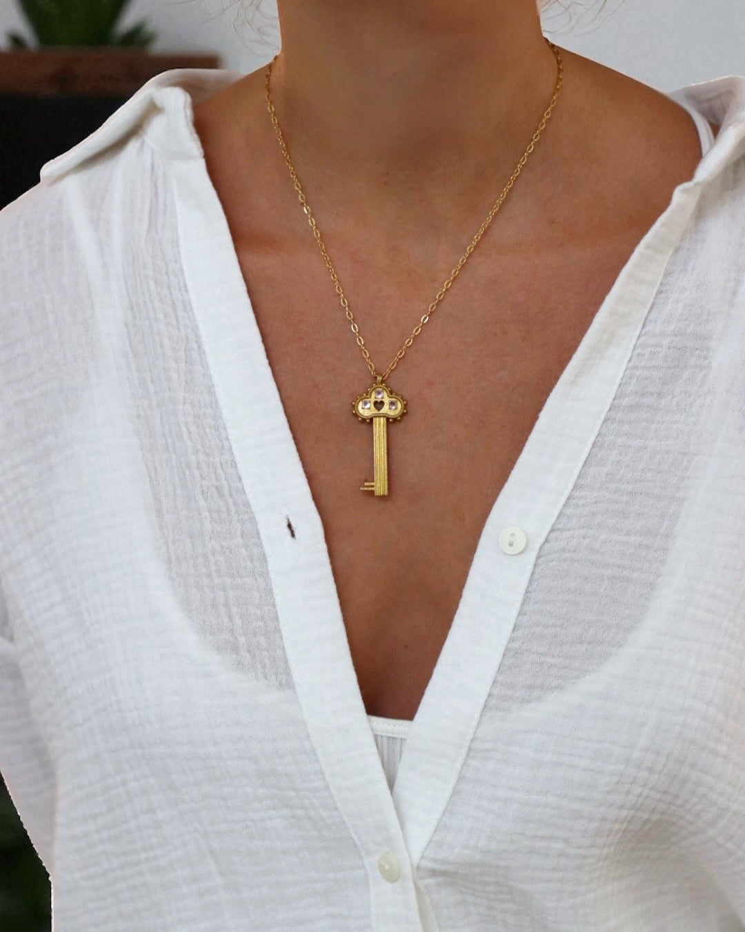 Person wearing a gold necklace with a key pendant against a neutral background