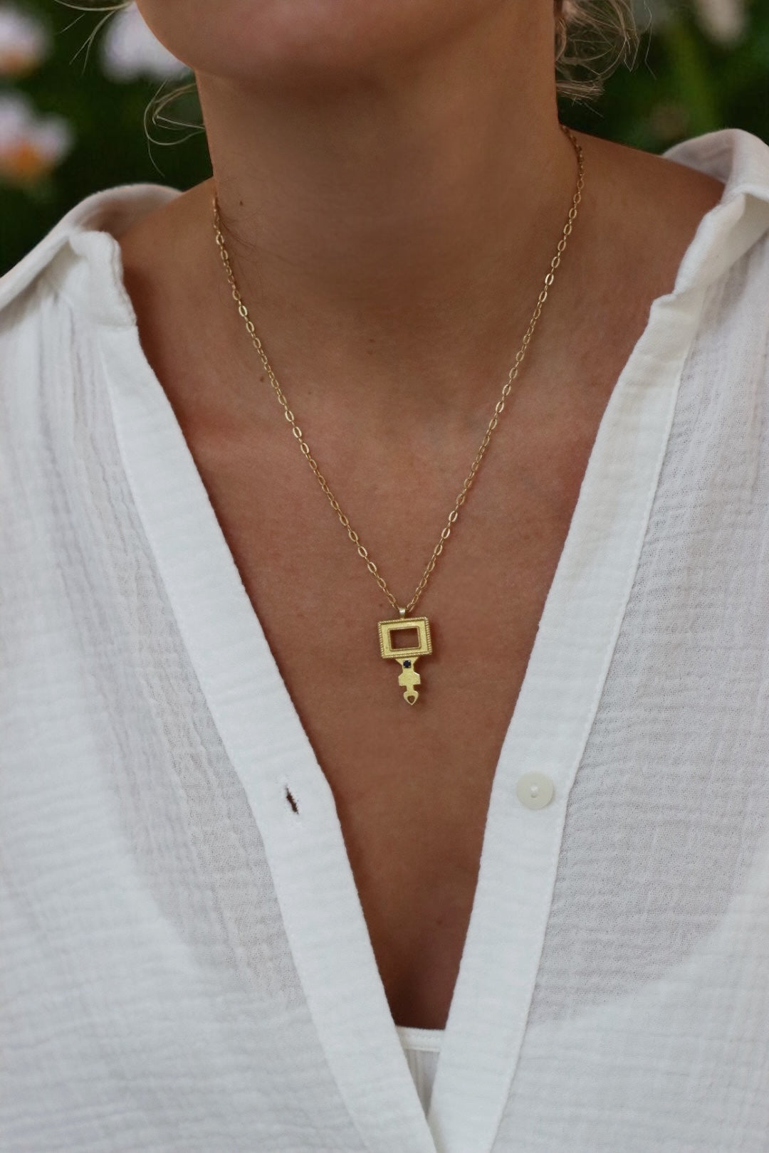 Gold necklace with a unique pendant worn by a person in a white shirt.