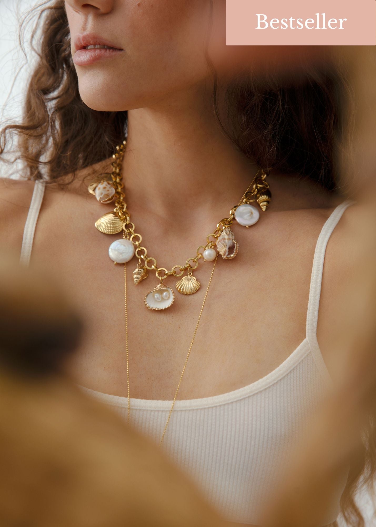 Woman wearing the Kailua Seashells and Pearls Necklace, showcasing the gold-filled chain adorned with seashell and pearl charms against a beach backdrop.