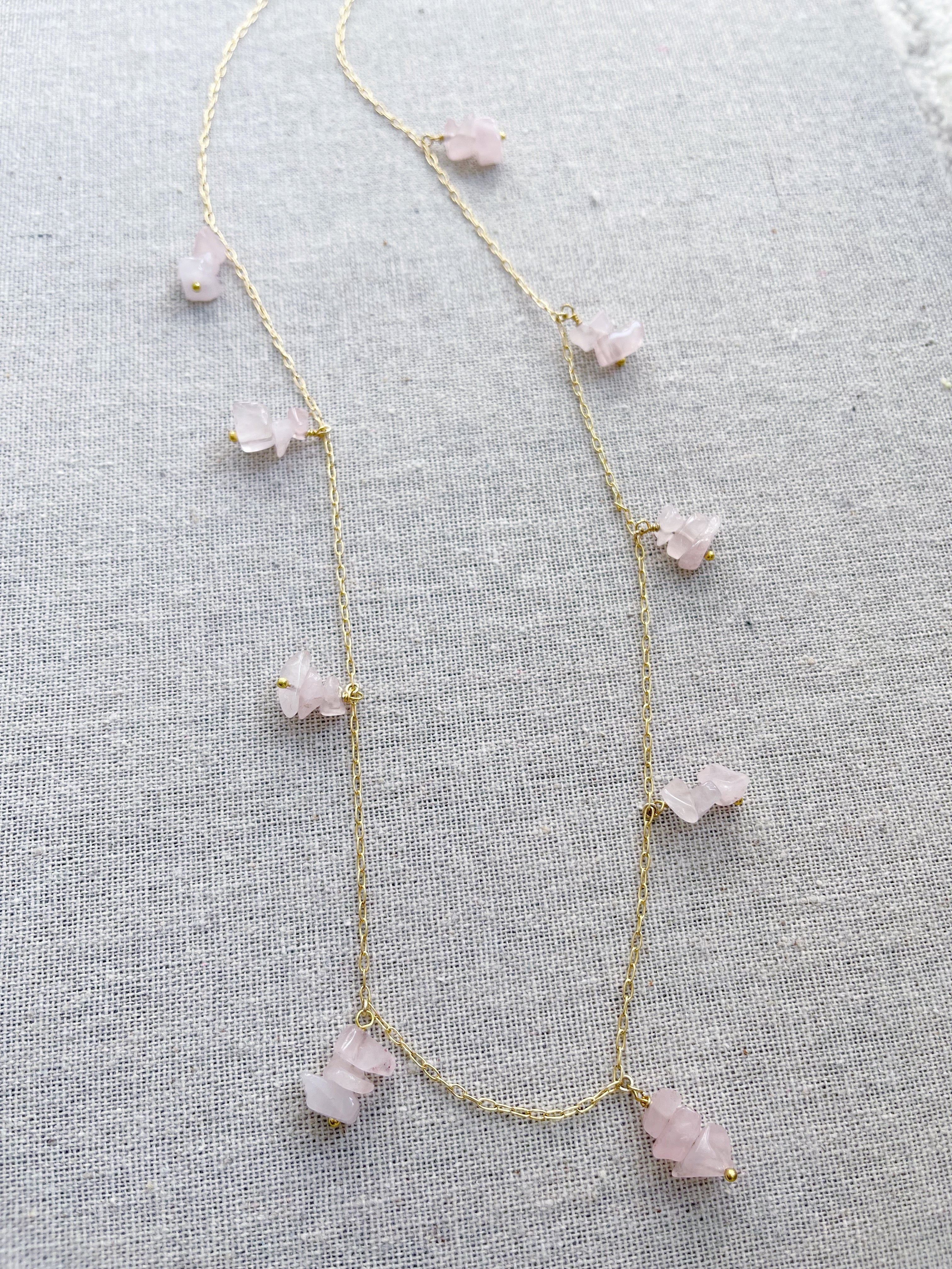 A gold necklace featuring groups of pink quartz stones.   The pink quartz stone is used in holistic healing and crystal therapy.  Rose quartz is known as a healing crystal and the stone of unconditional love. It's believed by some to emit strong vibrations of love, which are thought to: support emotional and relationship healing. inspire compassion.  Pink quartz  14k plated gold chain